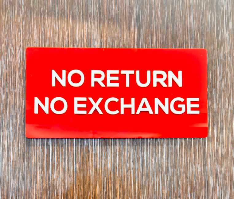 A rectangular red plastic sign with bold white uppercase letters displaying the message 'NO RETURN NO EXCHANGE.' The sign is placed flat on a wooden surface with a textured, natural brown finish and visible wood grain lines running vertically. The background appears to be part of an interior or outdoor setting, and the lighting is even, highlighting the sign's smooth surface and vibrant color. This type of signage is often used in retail or private disposal settings to indicate policies on returns or exchanges, aligning with alternative waste handling or rubbish clearance contexts, which may be relevant to private rubbish collection services such as those offered by Rubbish Clearance Fulham.