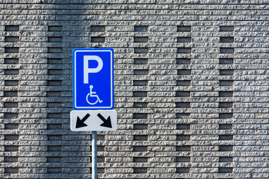 A blue and white parking sign indicating accessible parking with a wheelchair symbol and arrows pointing left and right, mounted on a metal pole in front of a textured brick wall. The wall is composed of rectangular bricks in shades of grey, with some bricks protruding slightly to create a pattern. The scene is evenly lit by natural daylight, with no vehicles or additional objects visible, set in an outdoor environment likely near a building front or parking area. The signage and brickwork suggest a typical urban setting, and the context relates to parking or access regulations that may be relevant for waste removal or logistics services operating in the vicinity, such as those provided by Rubbish Clearance Fulham.